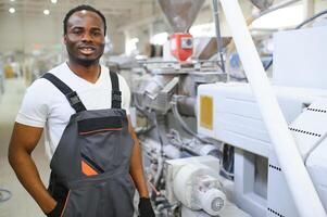 ritratto di africano americano maschio ingegnere nel uniforme e in piedi nel industriale fabbrica foto