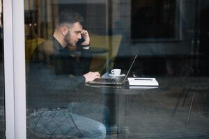 giovane uomo d'affari parlando su mobile Telefono mentre Lavorando su il computer portatile nel bar. foto