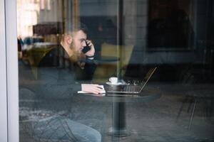 giovane uomo d'affari parlando su mobile Telefono mentre Lavorando su il computer portatile nel bar. foto