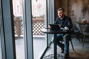 bello uomo d'affari utilizzando un' digitale tavoletta e potabile caffè mentre seduta nel bar nel il città centro. foto