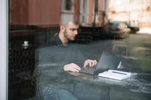 giovane riuscito uomo d'affari Lavorando su un' il computer portatile mentre seduta nel bar foto