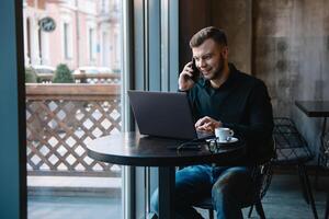 giovane uomo d'affari parlando su mobile Telefono mentre Lavorando su il computer portatile nel bar. foto