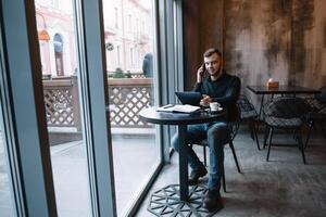 giovane uomo d'affari parlando su mobile Telefono mentre Lavorando su tavoletta nel bar. foto