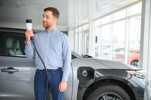 giovane uomo, vendita elettrico macchine nel il showroom. concetto di acquisto eco-friendly auto per famiglia foto