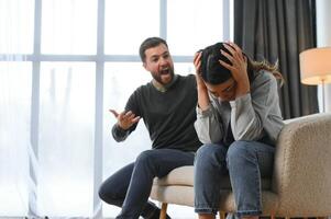 emotivo uomo Esprimere a gesti e urlando a il suo moglie, giovane coppia avendo litigare a casa. domestico abuso concetto foto
