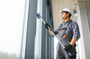 maschio professionale pulizia servizio lavoratore nel tuta da lavoro pulisce il finestre e negozio finestre foto