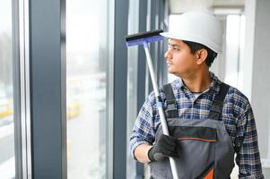 maschio professionale pulizia servizio lavoratore nel tuta da lavoro pulisce il finestre e negozio finestre foto