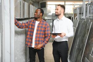 africano uomo la scelta ceramica piastrelle e utensili per il suo casa bagno e maschio venditore aiuta lui per rendere giusto decisione foto