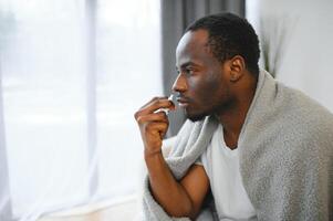 freddo e influenza trattamento. malato africano americano uomo utilizzando nasale spray foto