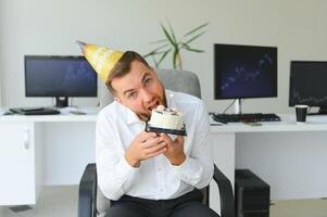 giovane contento uomo d'affari festeggiare il suo compleanno nel il ufficio. lui detiene un' torta nel il suo mani. foto