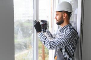 operaio nel tuta da lavoro installazione o regolazione plastica finestre nel il vivente camera a casa foto