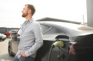 un' uomo addebiti il suo moderno elettrico macchina. il concetto di verde energia foto