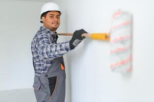 un indiano appartamento riparazione lavoratore vernici un' bianca parete con un' rullo. foto
