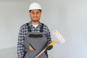 un indiano appartamento riparazione lavoratore vernici un' bianca parete con un' rullo. foto