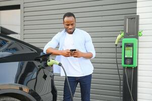 africano americano uomo ricarica il suo elettrico macchina. foto