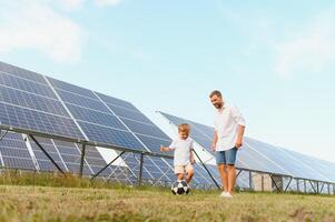 un' padre e il suo poco figlio giocare calcio vicino il solare pannelli. il concetto di rinnovabile energia. foto