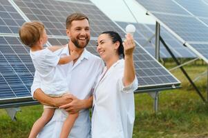 giovane famiglia di tre è accovacciato vicino fotovoltaico solare pannello, poco ragazzo e genitori. moderno famiglia concetto. il concetto di verde energia foto