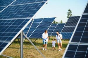 giovane famiglia di tre è accovacciato vicino fotovoltaico solare pannello, poco ragazzo e genitori. moderno famiglia concetto. il concetto di verde energia foto