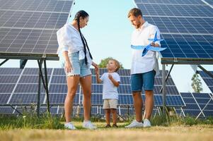 giovane famiglia di tre è accovacciato vicino fotovoltaico solare pannello, poco ragazzo e genitori. moderno famiglia concetto. il concetto di verde energia foto