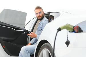 giovane elegante uomo è con elettrico auto a giorno. il concetto di verde energia foto