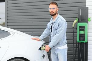 uomo Tenere energia ricarica cavo per elettrico auto nel all'aperto auto parco. e lui S andando per Collegare il auto per il ricarica stazione nel il parcheggio lotto vicino il shopping centro. foto