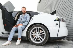 giovane elegante uomo è con elettrico auto a giorno. il concetto di verde energia foto