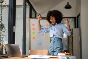 contento attività commerciale donna festeggiare vittoria mentre ricevente bene notizia su sua computer portatile, eccitato di successo. foto