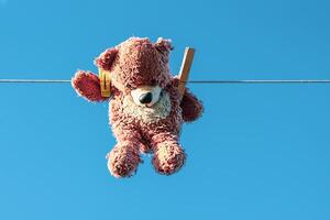 divertente Marrone orsacchiotto orso sospeso su un' clothesline con di legno molletta su blu cielo sfondo. foto