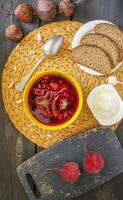rosso tradizionale russo e ucraino borscht o barbabietola la minestra con acida crema, aglio e aromi nel un' giallo ceramica tazza su di vimini tovaglietta sfondo. foto