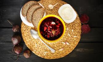 rosso tradizionale russo e ucraino borscht o barbabietola la minestra con acida crema, aglio e aromi nel un' giallo ceramica tazza su di vimini tovaglietta sfondo. foto