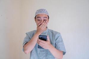 musulmano asiatico uomo sorpreso espressione guardare per smartphone quando Ramadan celebrazione. il foto è adatto per uso per Ramadhan manifesto e musulmano soddisfare media.