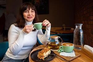 maturo donna con tazza di caldo tè e torta nel bar foto