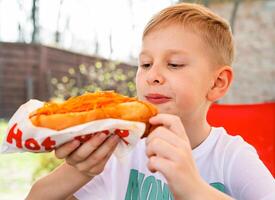 un' ragazzo mangia un' hot dog a un' tavolo nel un' bar nel un' primavera parco foto