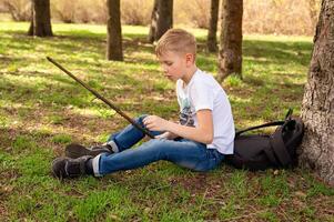 un' ragazzo con un' bastone si siede su il erba nel un' primavera parco foto