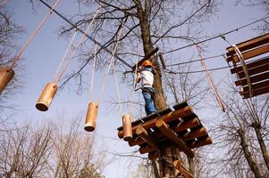 un' ragazzo nel un' casco si arrampica un' corda parco nel il primavera foto