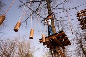 un' ragazzo nel un' casco si arrampica un' corda parco nel il primavera foto