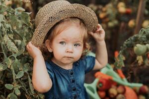 ritratto di un' carino poco ragazza nel un' blu vestito e un' cannuccia cappello nel il autunno giardino. giovane contadino foto