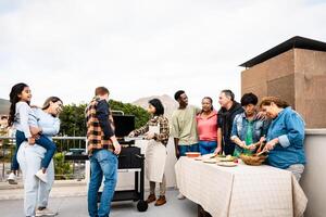 multigenerazionale amici avendo divertimento fare barbecue a Casa tetto - contento multirazziale persone cucinando insieme foto