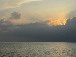 bellissimo tramonto su il mare, il sole imposta dietro a un' grande nube dire bugie su il acqua foto