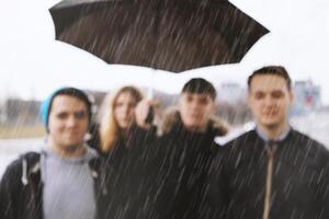 sfocato gruppo di giovane urbano adolescenziale amici sotto uno ombrello foto
