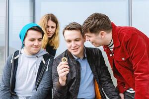 giovane uomo mostrando bitcoin moneta per il suo incuriosito gruppo di amici foto