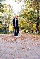 donna caucasica felice con il suo cane da riporto che cammina in un parco autunnale foto