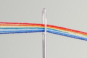multicolore discussioni per cucire nel il modulo di un' arcobaleno passaggio attraverso un antico ago su un' bianca sfondo foto