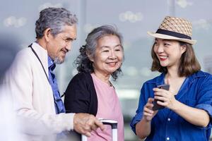 gruppo di asiatico famiglia turista passeggeri con anziano è utilizzando mobile applicazione per chiamata raccogliere su Taxi a aeroporto terminale per mezzi di trasporto durante il vacanza viaggio e lungo fine settimana vacanza foto