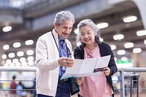 asiatico attivo anziano la pensione coppia è guardare a il carta geografica per direzione dentro aeroporto terminale per secondo luna di miele pensionato viaggio e urbano la metropolitana treno mezzi di trasporto concetto foto