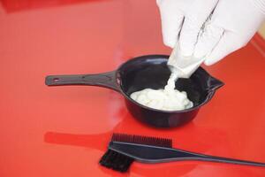 vicino su mani indossa guanti, spreme tintura capelli colore crema a partire dal tubo nel mescolare nel nero ciotola prima sta morendo del cliente capelli. concetto, capelli bellezza Prodotto per mutevole capelli colore di professionale parrucchiere. foto