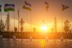 bandiere di Uzbekistan agitando su un' tramonto o Alba drammatico cielo sfondo. foto