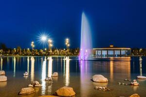 sfocato Fontana acqua flussi nel un artificiale lago nel un' notte parco con lanterne e decorazioni. foto