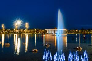 sfocato Fontana acqua flussi nel un artificiale lago nel un' notte parco con lanterne e decorazioni. foto