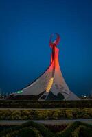 Uzbekistan, compito - Maggio 5, 2023 illuminato monumento di indipendenza nel il modulo di un' stele con un' humo uccello, fontane e agitando bandiere nel il nuovo Uzbekistan parco a notte. foto